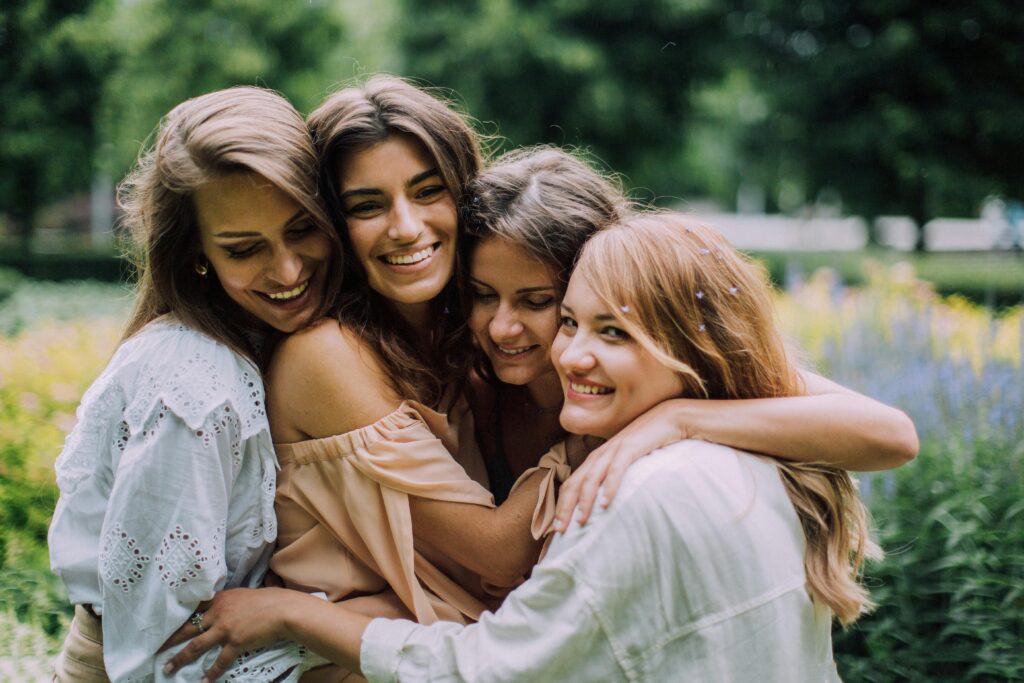 pexels-photo-4834142-4834142 Four smiling women joyfully embrace in a lush green park during summer, showcasing genuine friendship and happiness.